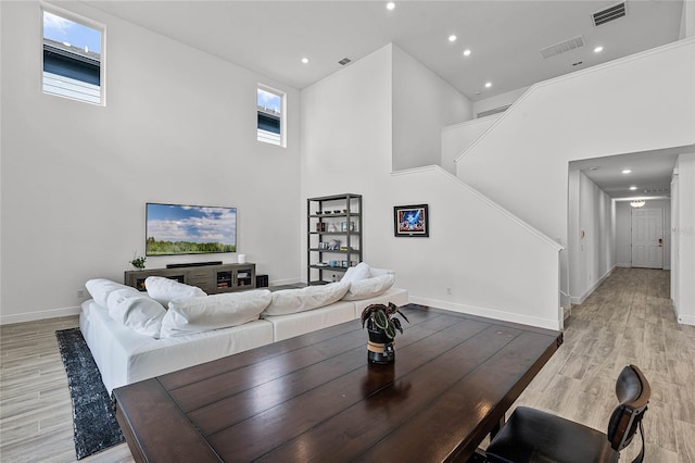 living room featuring light wood-type flooring, visible vents, and a towering ceiling