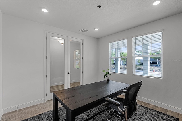 office area with light wood-style floors, baseboards, visible vents, and a textured ceiling