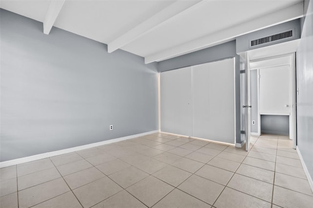 interior space with light tile patterned floors, beam ceiling, and a closet