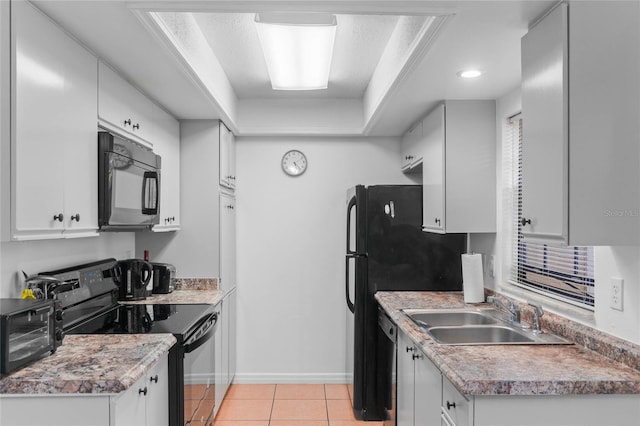 kitchen with a tray ceiling, sink, black appliances, white cabinetry, and light tile patterned flooring