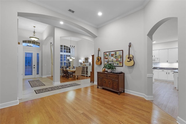 entrance foyer with a high ceiling, light wood-type flooring, an inviting chandelier, and crown molding