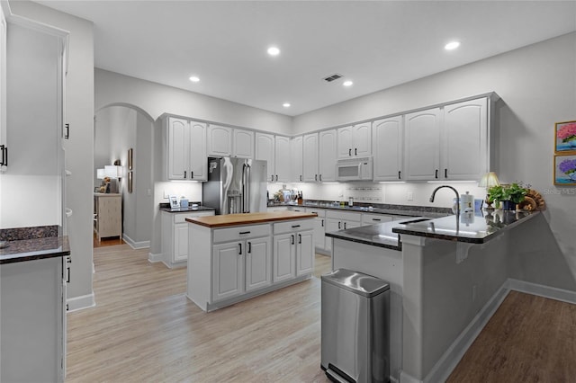 kitchen with white cabinetry, sink, wooden counters, stainless steel refrigerator with ice dispenser, and kitchen peninsula