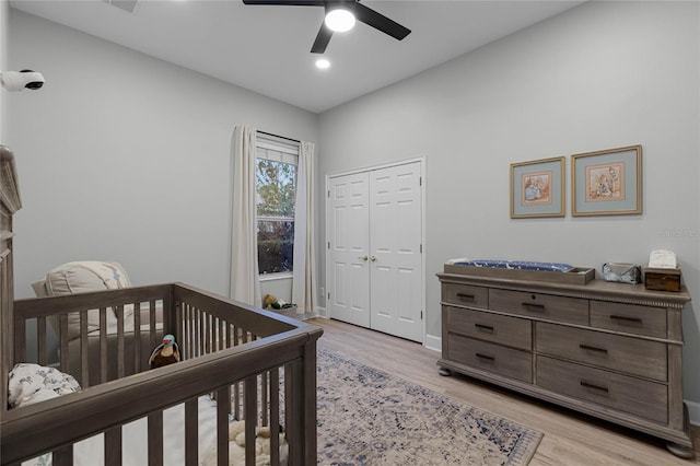 bedroom with ceiling fan, a closet, a nursery area, and light wood-type flooring