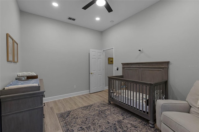 bedroom with ceiling fan, a towering ceiling, a nursery area, and light wood-type flooring