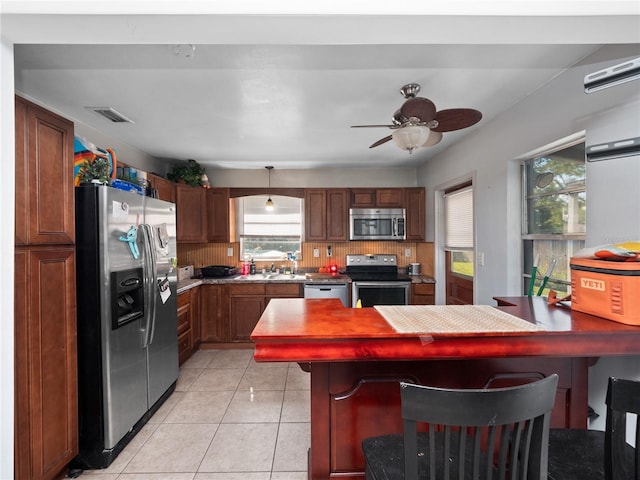 kitchen featuring ceiling fan, a breakfast bar area, decorative backsplash, light tile patterned floors, and appliances with stainless steel finishes