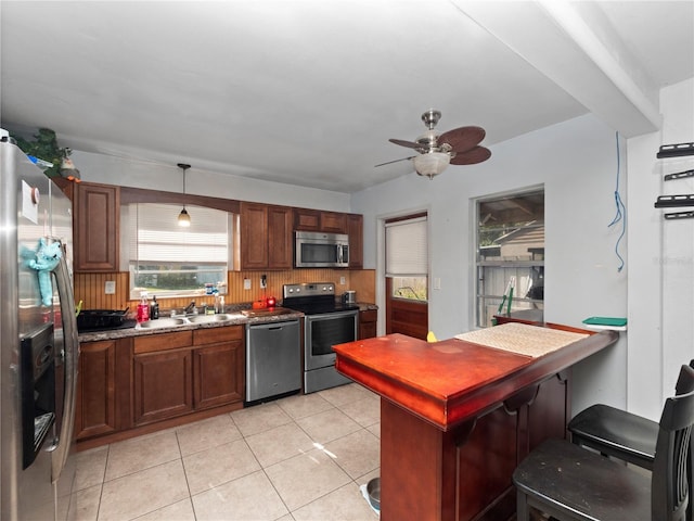 kitchen with appliances with stainless steel finishes, backsplash, ceiling fan, light tile patterned floors, and hanging light fixtures