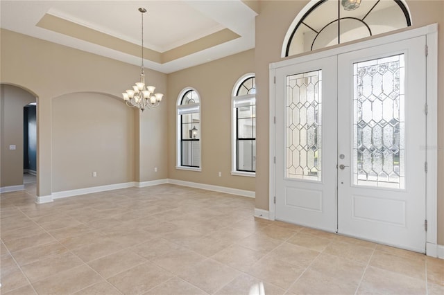 foyer entrance with a raised ceiling, crown molding, light tile patterned floors, and a notable chandelier