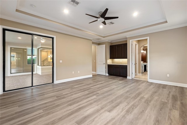 unfurnished living room with ceiling fan, light wood-type flooring, ornamental molding, and a tray ceiling