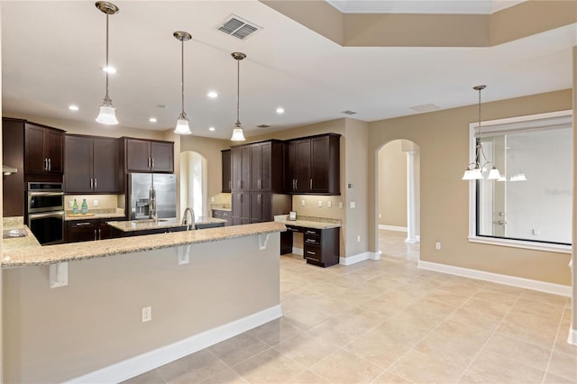 kitchen with pendant lighting, light stone counters, dark brown cabinetry, a breakfast bar area, and stainless steel appliances