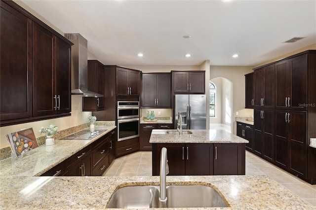 kitchen featuring light stone countertops, sink, stainless steel appliances, and wall chimney range hood