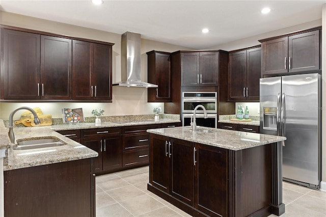 kitchen featuring sink, wall chimney range hood, stainless steel appliances, and a kitchen island with sink