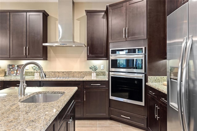 kitchen with light stone countertops, stainless steel appliances, wall chimney range hood, dark brown cabinets, and light tile patterned flooring