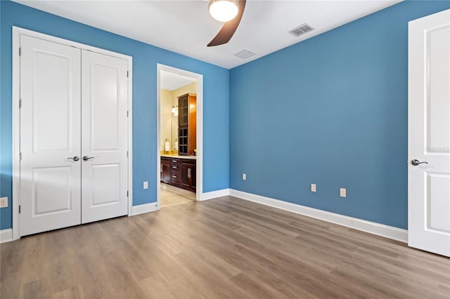 unfurnished bedroom featuring hardwood / wood-style floors, ceiling fan, connected bathroom, and a closet