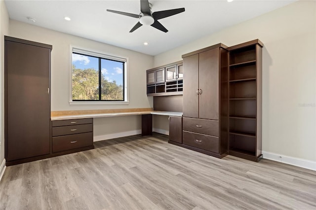 unfurnished office featuring ceiling fan, light wood-type flooring, and built in desk