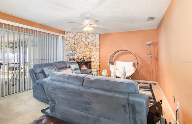 carpeted living room with ceiling fan, a stone fireplace, and a textured ceiling