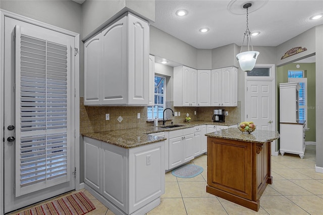 kitchen with white cabinetry, sink, pendant lighting, and light stone countertops