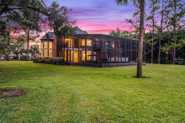 back house at dusk with glass enclosure and a yard