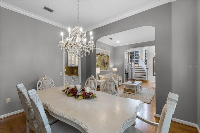 dining room featuring crown molding, arched walkways, stairs, wood finished floors, and visible vents