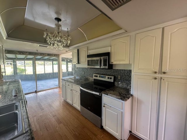 kitchen with dark stone counters, appliances with stainless steel finishes, a raised ceiling, pendant lighting, and white cabinets