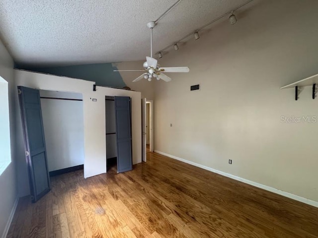 unfurnished bedroom with a textured ceiling, hardwood / wood-style floors, vaulted ceiling, two closets, and ceiling fan