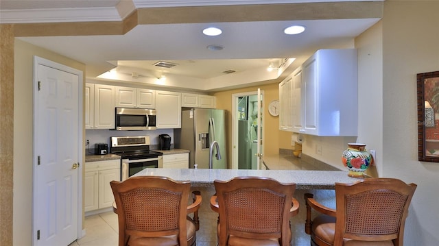 kitchen with white cabinetry, a tray ceiling, light tile patterned floors, and stainless steel appliances