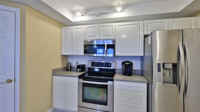 kitchen with a tray ceiling, appliances with stainless steel finishes, decorative backsplash, and white cabinets