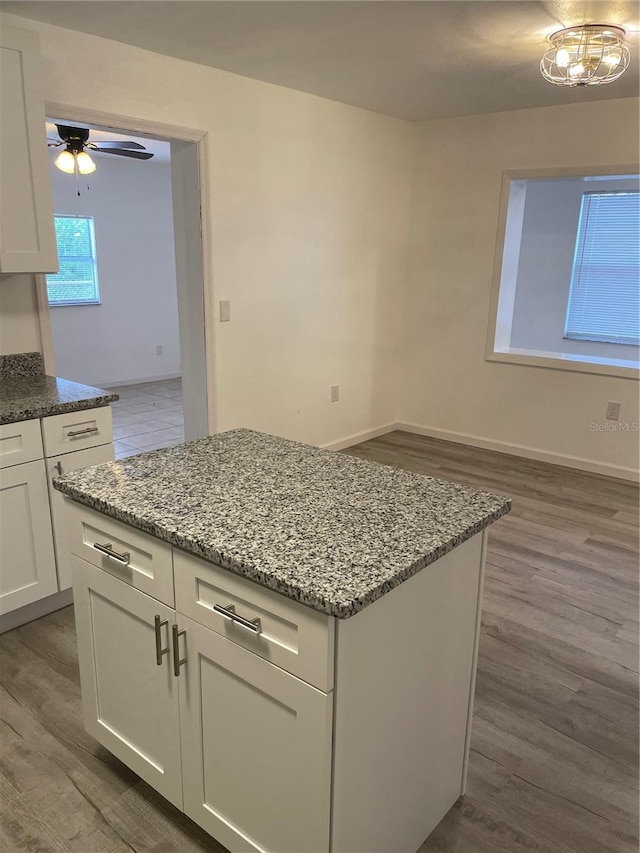 kitchen featuring light stone counters, a kitchen island, white cabinetry, dark wood-type flooring, and ceiling fan