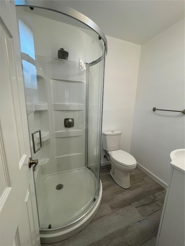 bathroom featuring toilet, vanity, wood-type flooring, and a shower with door