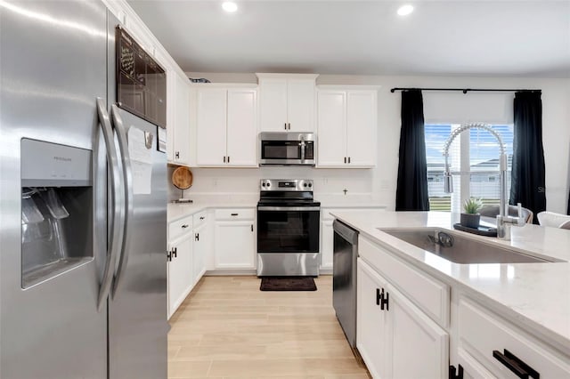 kitchen featuring appliances with stainless steel finishes, white cabinetry, sink, light stone counters, and light hardwood / wood-style floors