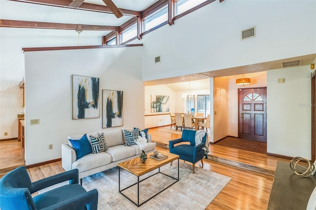 living room with beamed ceiling, light hardwood / wood-style floors, high vaulted ceiling, and a chandelier