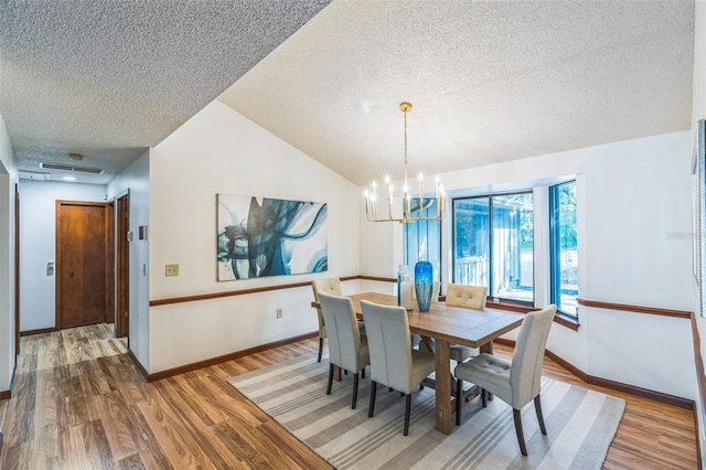 dining room featuring a textured ceiling, hardwood / wood-style flooring, vaulted ceiling, and an inviting chandelier