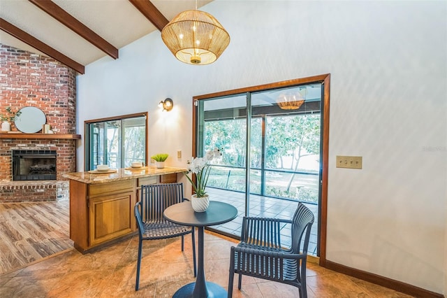 dining area with beam ceiling, light hardwood / wood-style floors, high vaulted ceiling, and a brick fireplace