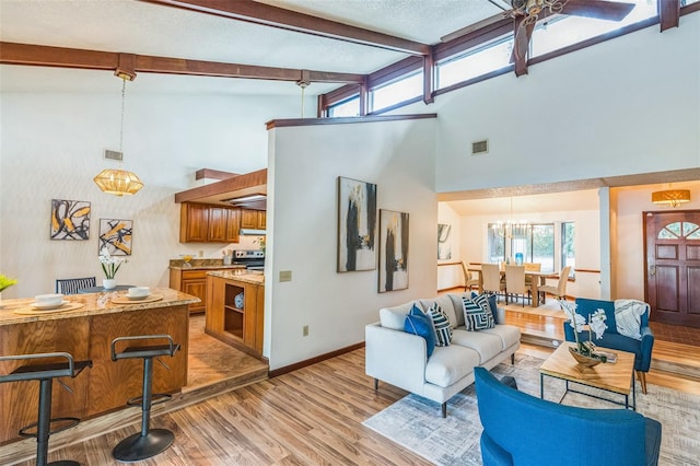 living room with beam ceiling, ceiling fan with notable chandelier, light hardwood / wood-style floors, and high vaulted ceiling