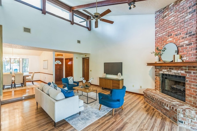 living room with a brick fireplace, ceiling fan with notable chandelier, high vaulted ceiling, and light hardwood / wood-style flooring