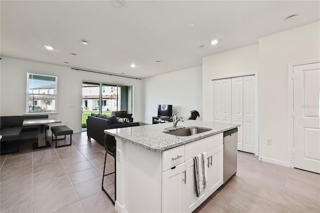 kitchen featuring a center island with sink, white cabinets, sink, stainless steel dishwasher, and light stone countertops