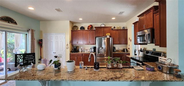 kitchen with kitchen peninsula, a kitchen bar, stainless steel appliances, and light stone counters