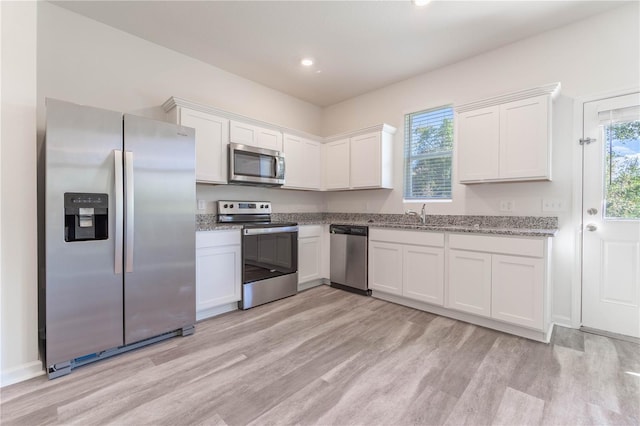 kitchen with stainless steel appliances, white cabinetry, and light hardwood / wood-style floors