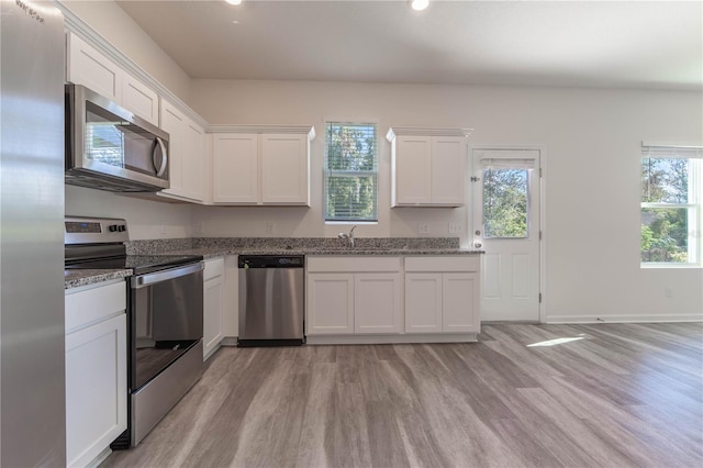 kitchen with white cabinets, appliances with stainless steel finishes, light hardwood / wood-style floors, and stone countertops