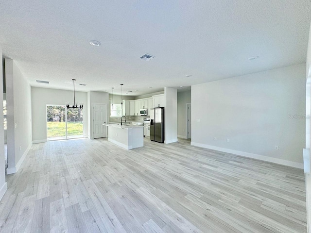 unfurnished living room with light hardwood / wood-style floors, a chandelier, a textured ceiling, and sink