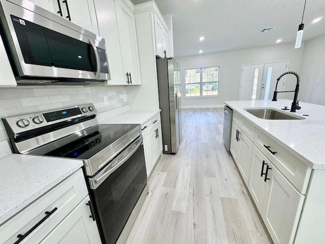 kitchen with white cabinets, appliances with stainless steel finishes, sink, and light stone countertops