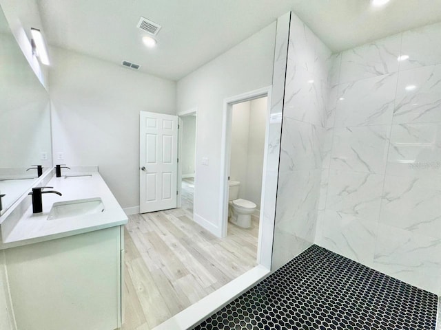 bathroom featuring wood-type flooring, vanity, toilet, and tiled shower