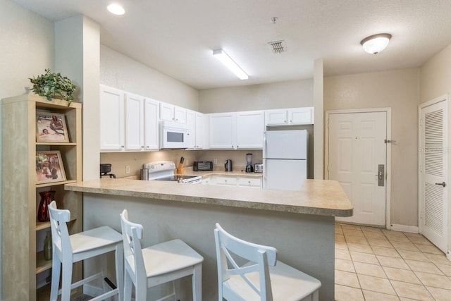 kitchen featuring light tile patterned flooring, white cabinetry, kitchen peninsula, a breakfast bar area, and white appliances