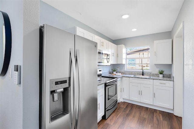 kitchen with a sink, light stone counters, stainless steel appliances, white cabinetry, and dark wood-style flooring