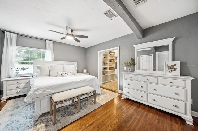 bedroom with a spacious closet, ceiling fan, dark hardwood / wood-style flooring, beamed ceiling, and a closet