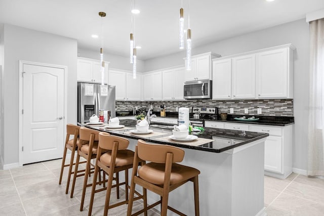 kitchen with decorative backsplash, stainless steel appliances, a center island with sink, white cabinetry, and hanging light fixtures