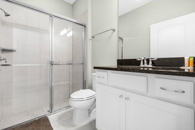 bathroom featuring toilet, vanity, tile patterned floors, and a shower with shower door