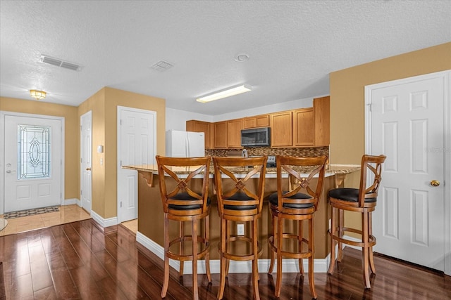 kitchen featuring kitchen peninsula, dark hardwood / wood-style flooring, a breakfast bar, a textured ceiling, and white refrigerator