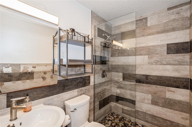 bathroom featuring sink, a textured ceiling, tiled shower, toilet, and tile walls