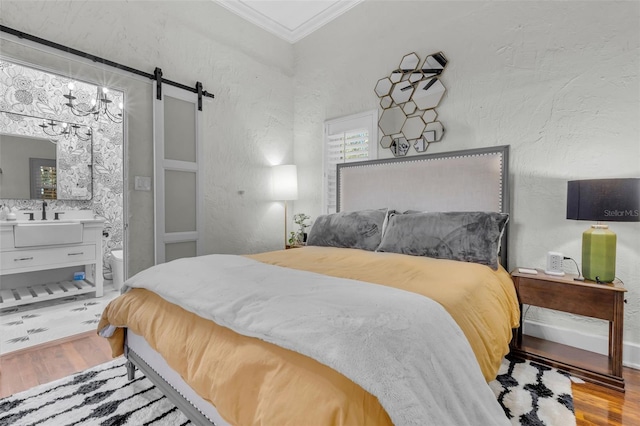 bedroom featuring light wood-type flooring, crown molding, sink, a barn door, and connected bathroom