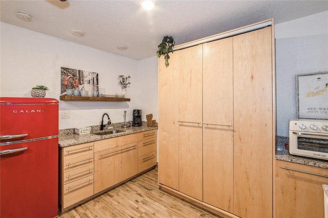 kitchen featuring refrigerator, sink, light stone countertops, light brown cabinetry, and light hardwood / wood-style floors